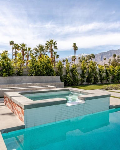 Modern backyard with turquoise swimming pool, spa, concrete seating areas, palm trees, and mountain views