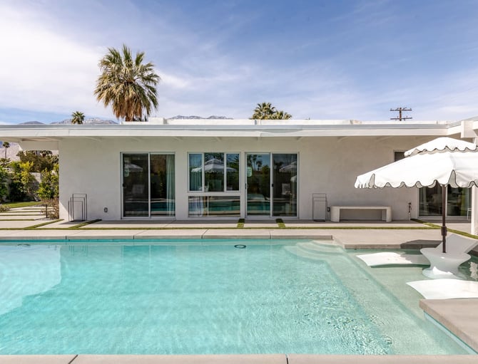 Modern white house with pool, lounge chairs, white umbrellas, and mountain views in desert landscape